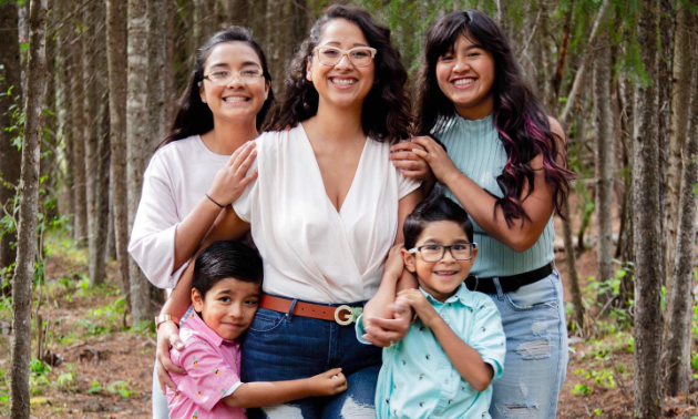 Luz Hernandez and her four children smile while hugging each other.