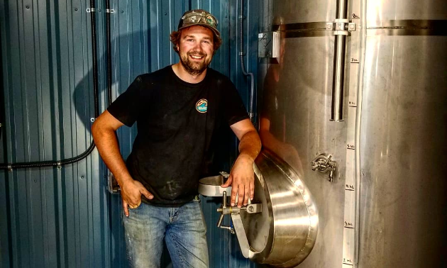 Hedin Nelson-Chorney, owner of Tailout Brewing, leaning against brewery tank. 