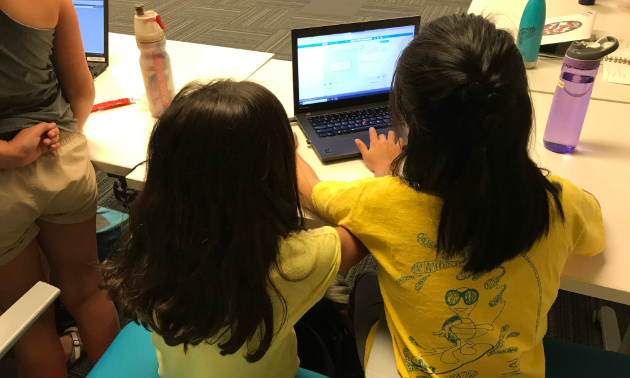 Two kids in yellow shirts interact with a computer.