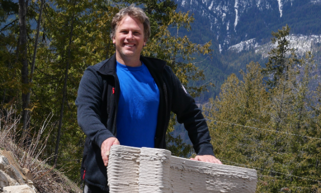 Ian Comishin smiles in front of a stack of printed concrete.