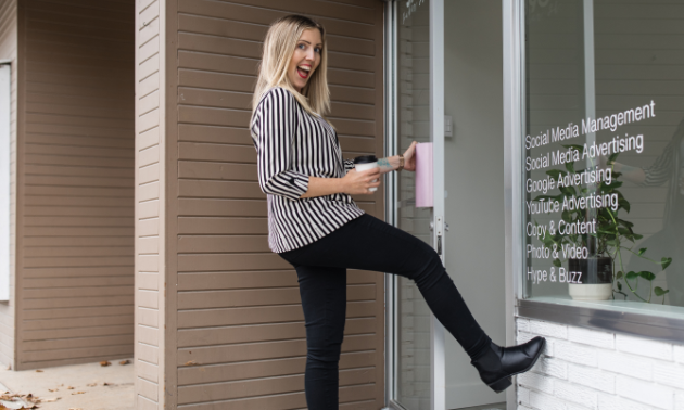 Zan Comerford smiles while kicking her leg up to open the door to her business, Liteworks Marketing. 