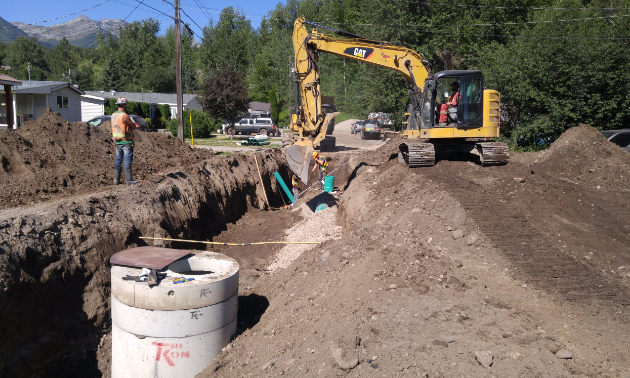 An excavator digs a deep trench where a road used to be.