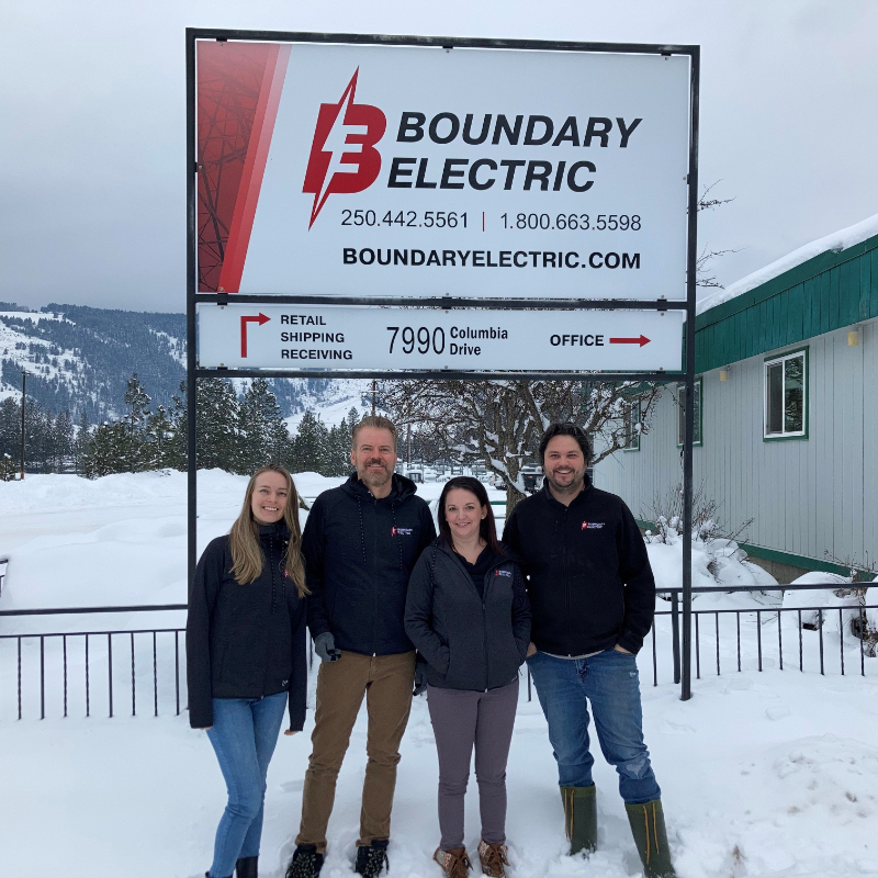 Four employees stand in front of a Boundary Electric sign in Grand Forks, B.C.