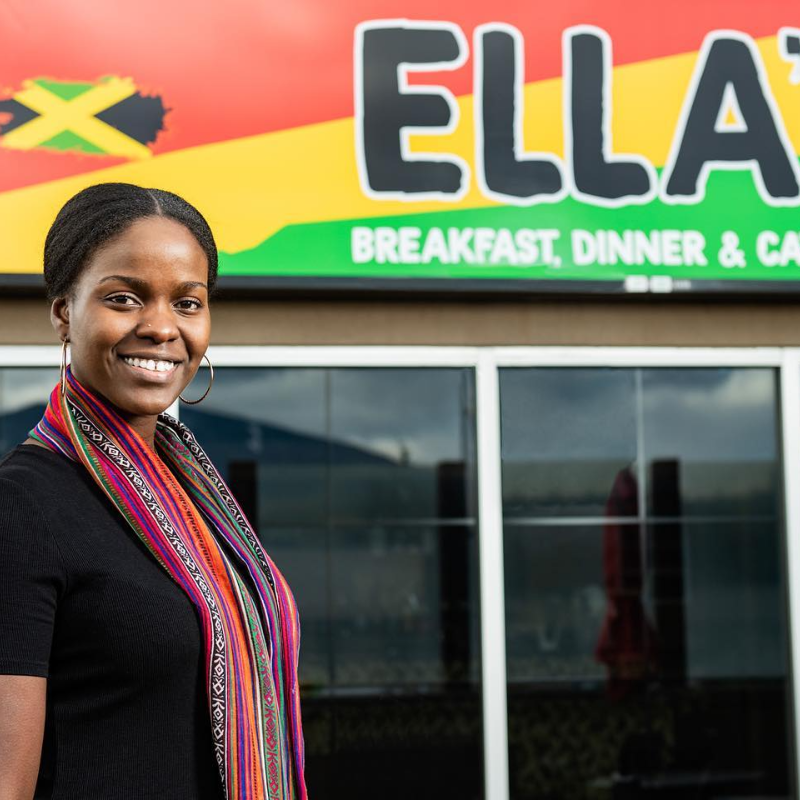 Aleitha Harvey smiles in front of her sign for her restaurant, Ella’s. 