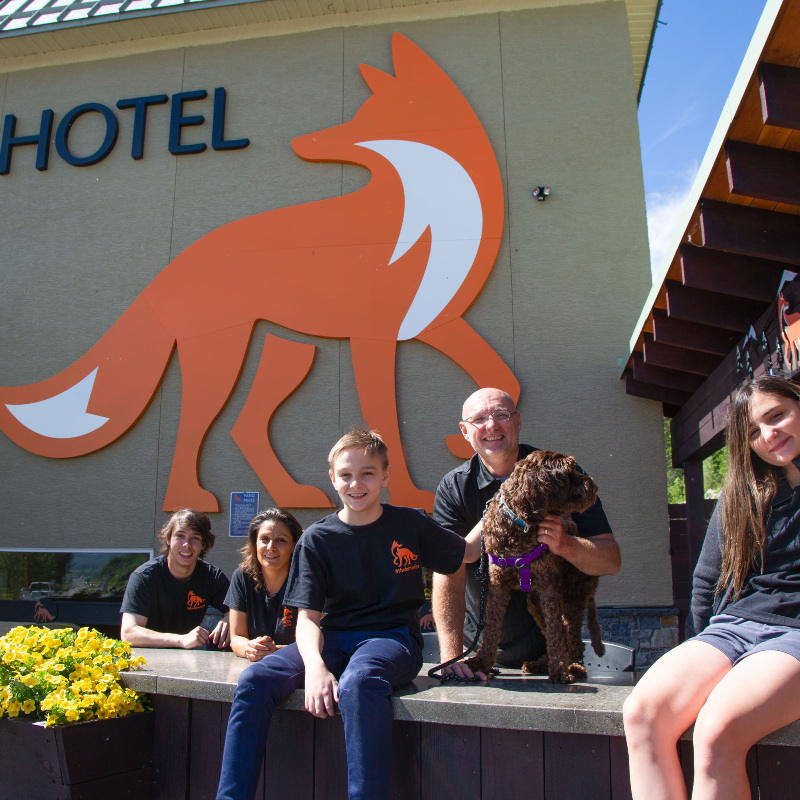 (L to R) Mackenzie, Marina, Jayden, Jeremiah and Maya Pauw in front of a hotel with a big bright orange image of a fox. 