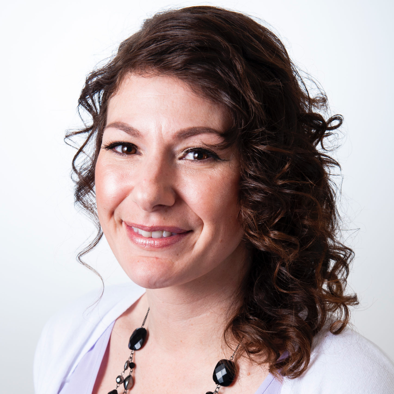 Helen Barron smiles. She has long curly brown hair and wears a white shirt. 