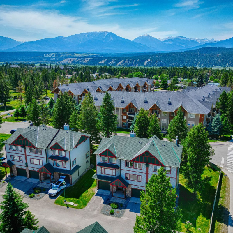An aerial view of the Columbia Valley showcases some pristine, tall homes among trees and distant mountains. 