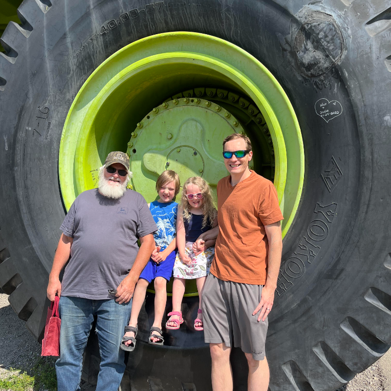 The green Terex Titan dump truck is parked with John, Kyle, Annabelle, and Gus Born standing in front of it. 