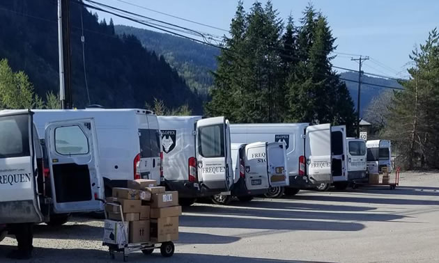 Alopex trucks in Castlegar are getting loaded up for delivery. Shown are a line of parked trucks and packages on a cart.