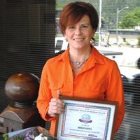 Amber Hayes stands holding a bouquet and her Influential Women in Business award certificate.