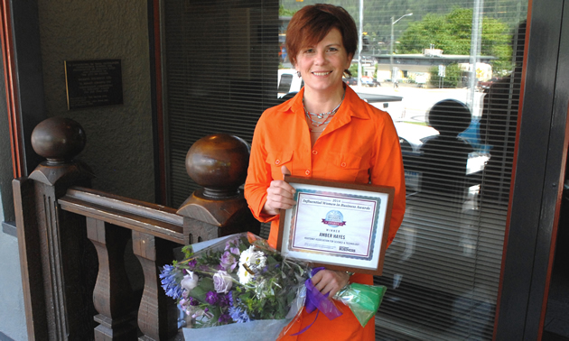 Amber Hayes stands holding a bouquet and her Influential Women in Business award certificate.