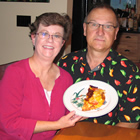 Man and woman sit at a kitchen table, holding up a plate with half of a frittata