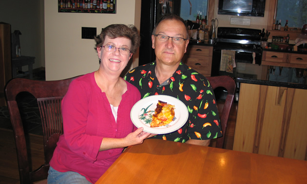 Man and woman sit at a kitchen table, holding up a plate with half of a frittata