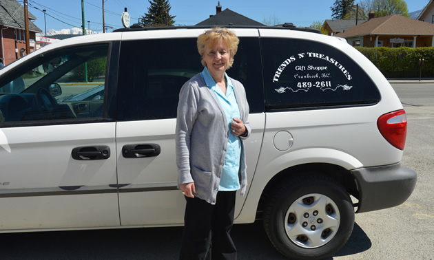 Senior woman stands beside a white mini-van