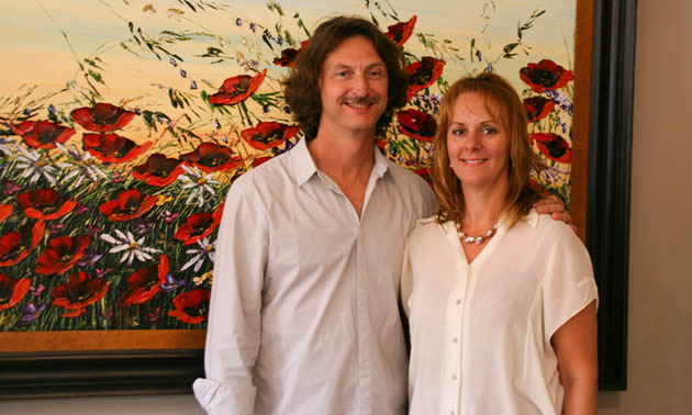 Smiling couple standing in front of a large painting of wind-blown red poppies