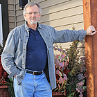 Middle-aged man in casual clothes stands outside the doorway of a multi-unit dwelling.