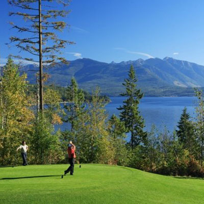 Two people teeing off on lakeside course. 