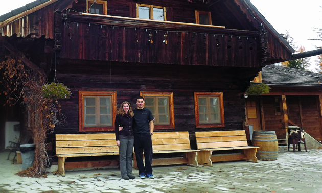 young couple standing in front of a large rustic wooden building