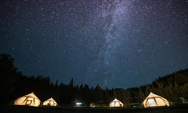 A night shot of the Milky Way with illuminated tents below. 