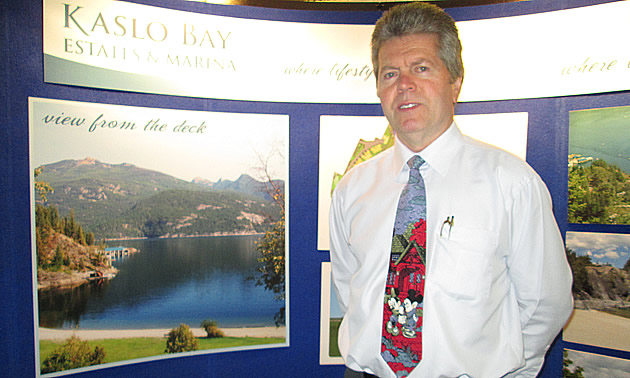 Gray-haired man in white shirt and tie stands in front of a curved photo display