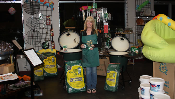 Margeaux Bauman, co-owner of Kootenay Valley Water & Spas, is standing with the Big Green Egg barbecue and a big bag of natural charcoal.