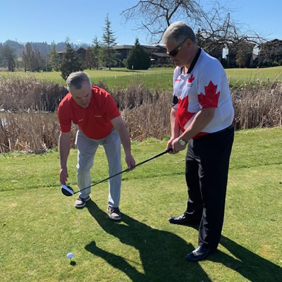 A blind golf competitor uses the assistance of a coach as he sets up a shot.