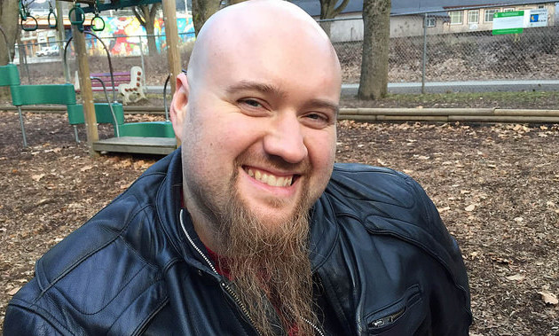 Brad Pommen smiles for a photo. He wears a black leather jacket and has a long brown goatee. 