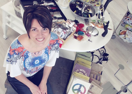 Brandy, wearing printed shirt and short black hair, sits in front of a table containing watches and jewellery for sale.