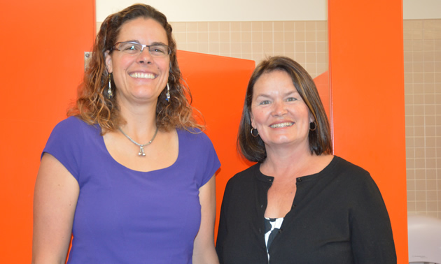 Two smiling women standing in front of orange bathroom doors