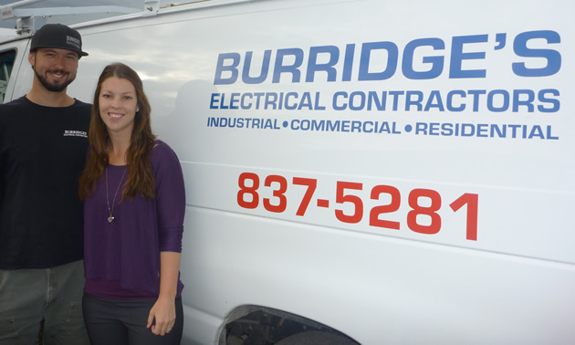 Smiling young couple stands beside a white van bearing the name Burridge's Electrical Contractors 