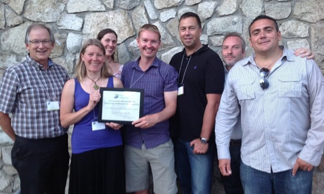 A group stands together displaying a framed certificate.