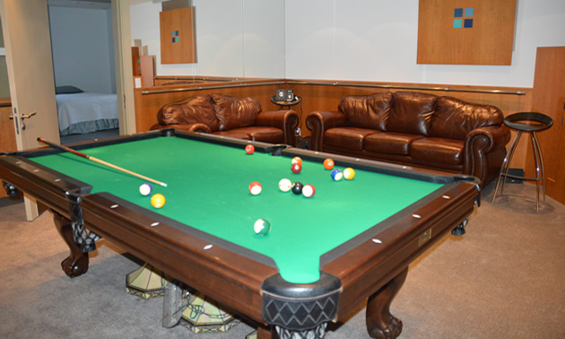 Billiard table in a room with leather chairs lining one wall