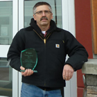 Man holding a clear acrylic trophy stands in front of the Creston & District Community Complex