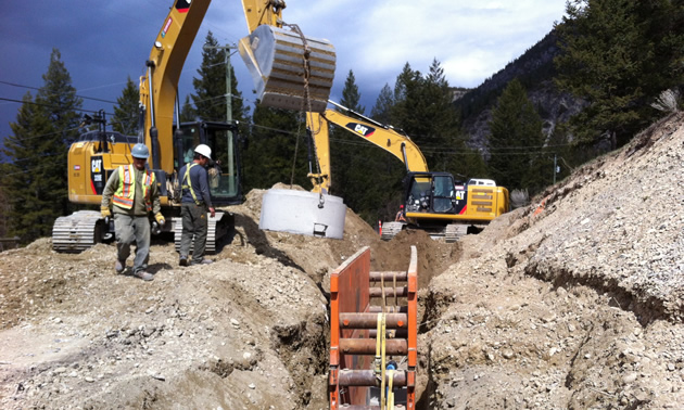 Earth moving equipment, a trench holding a metal framework, and a few workers