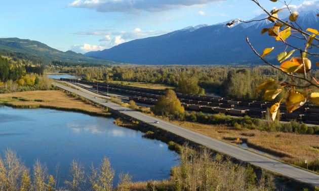 Highway near Golden, B.C., with a field of railway coal cars on one side and wetlands on the other