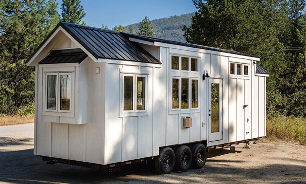 White tiny home sitting on gravel road. 