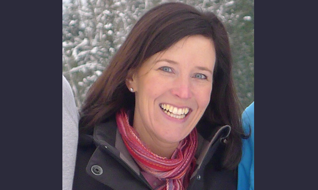 Christine Andison stands next to family in a winter environment, she wears a black jacket and pink and red scarf.