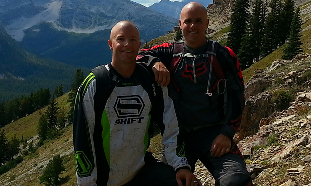 Two young men standing side by side on a mountain slope on a sunny summer day