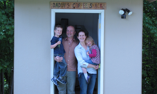 Man and woman, each holding a child, stand in the doorway of a small structure with a sign saying 