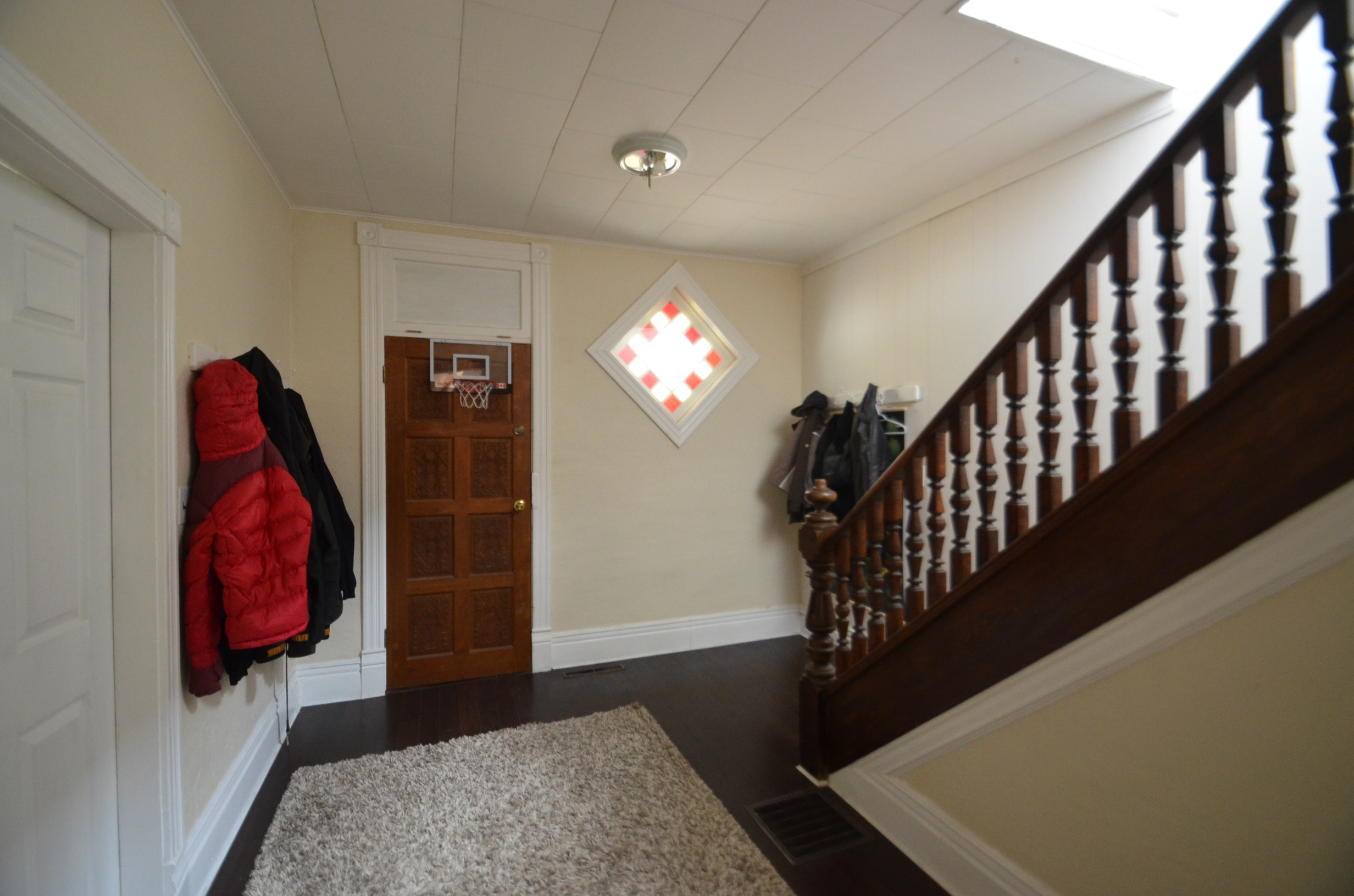 A front entry with a coat rack full of coats, a basketball hoop over the door and a rug on the floor. 