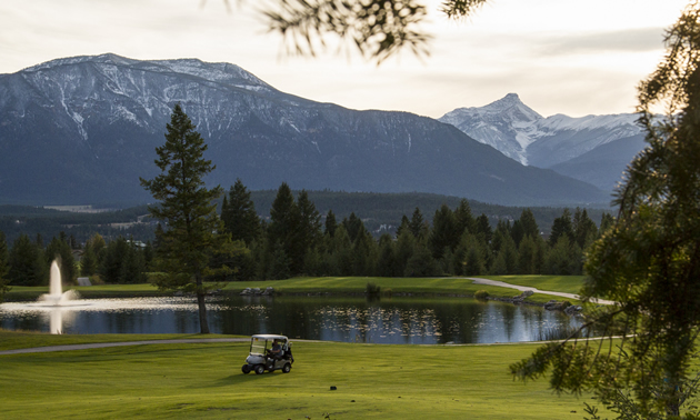 Golf course with golf cart, water feature and fountain, against a mountain backdrop