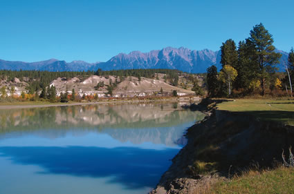 A flat-surfaced body of water with treed shoreline and mountains in distance