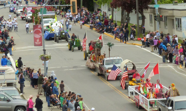 Parade goers line both sides of street as floats drive by. 