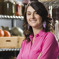 Young woman with long, dark hair, wearing a bright pink shirt, standing in a food market