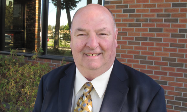 Senior man in a suit and tie standing in front of a windowed brick wall