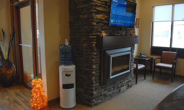 A gas fireplace beneath a television screen and comfortable chairs make up a waiting area.