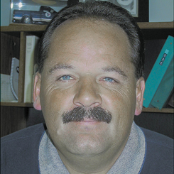 Dan, with mustache and collared shirt, smiles at the camera. 