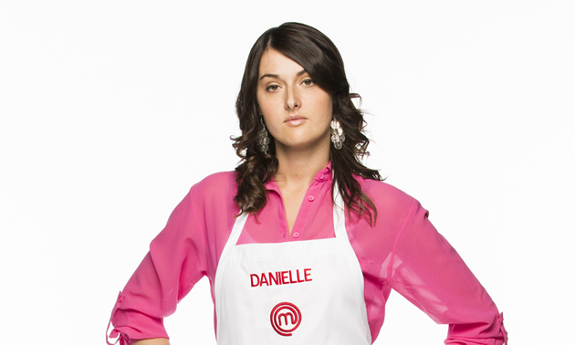 Dark-haired woman wearing a pink shirt and white chef's apron with the name Danielle on the bib