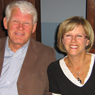 White-haired man and blonde woman smile warmly at the camera