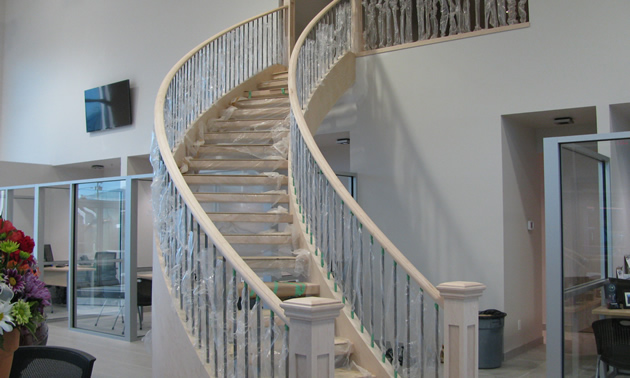 Curving staircase in pale wood, with plastic wrapping on the railing pickets
